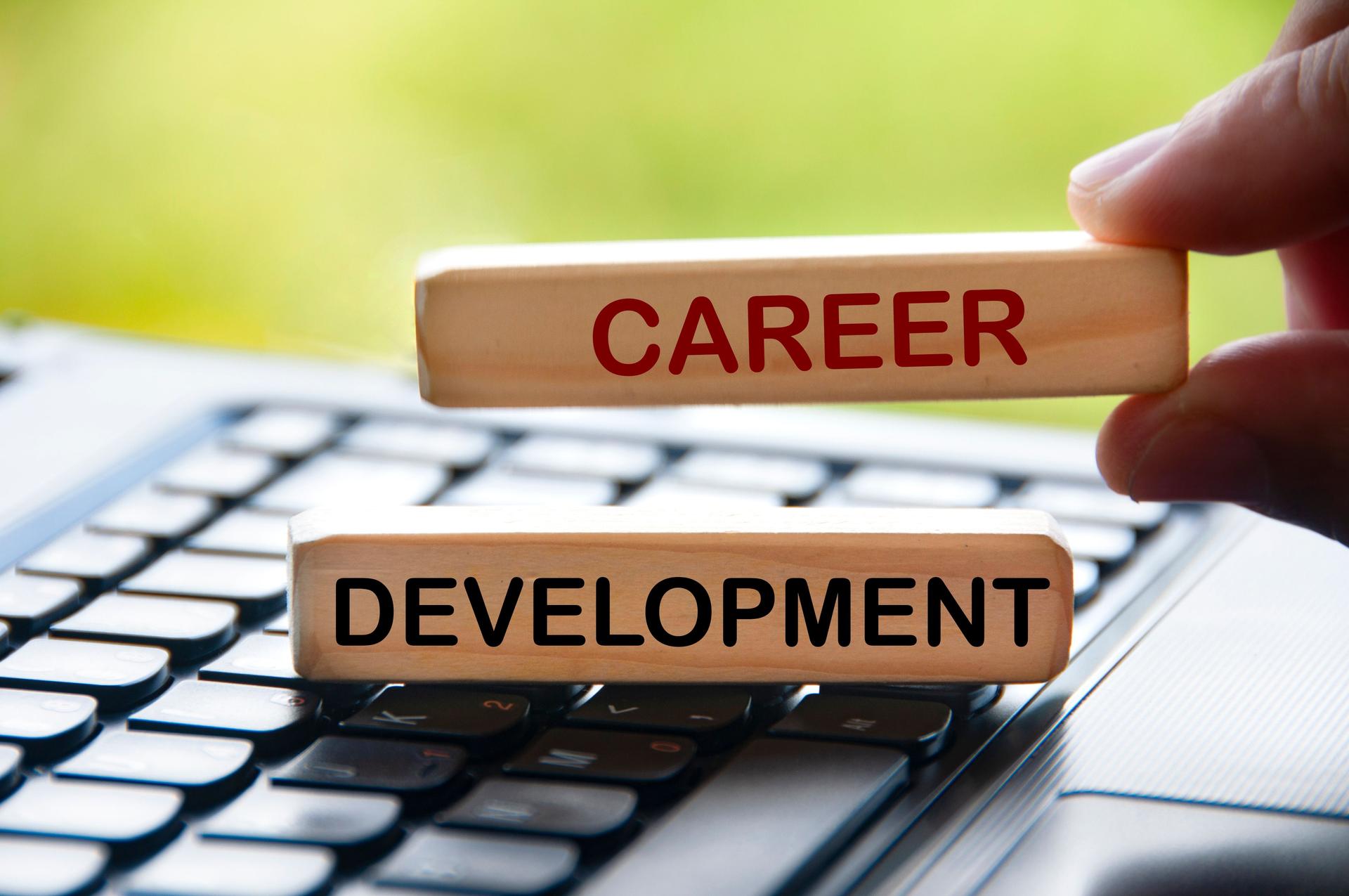 Hand holding wooden blocks with text on laptop keyboard - Career development.